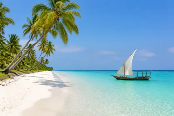 Biela pláž s palmami a tradičnou plachetnicou na Zanzibare